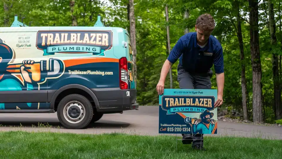 Trailblazer Plumbing tech in front of wrapped truck putting up yard sign in Lockport.